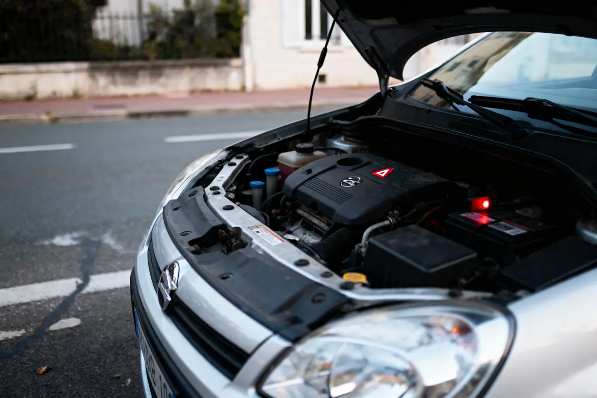 Capot de voiture ouvert, montrant le moteur d'un véhicule argenté stationné en bordure de route.