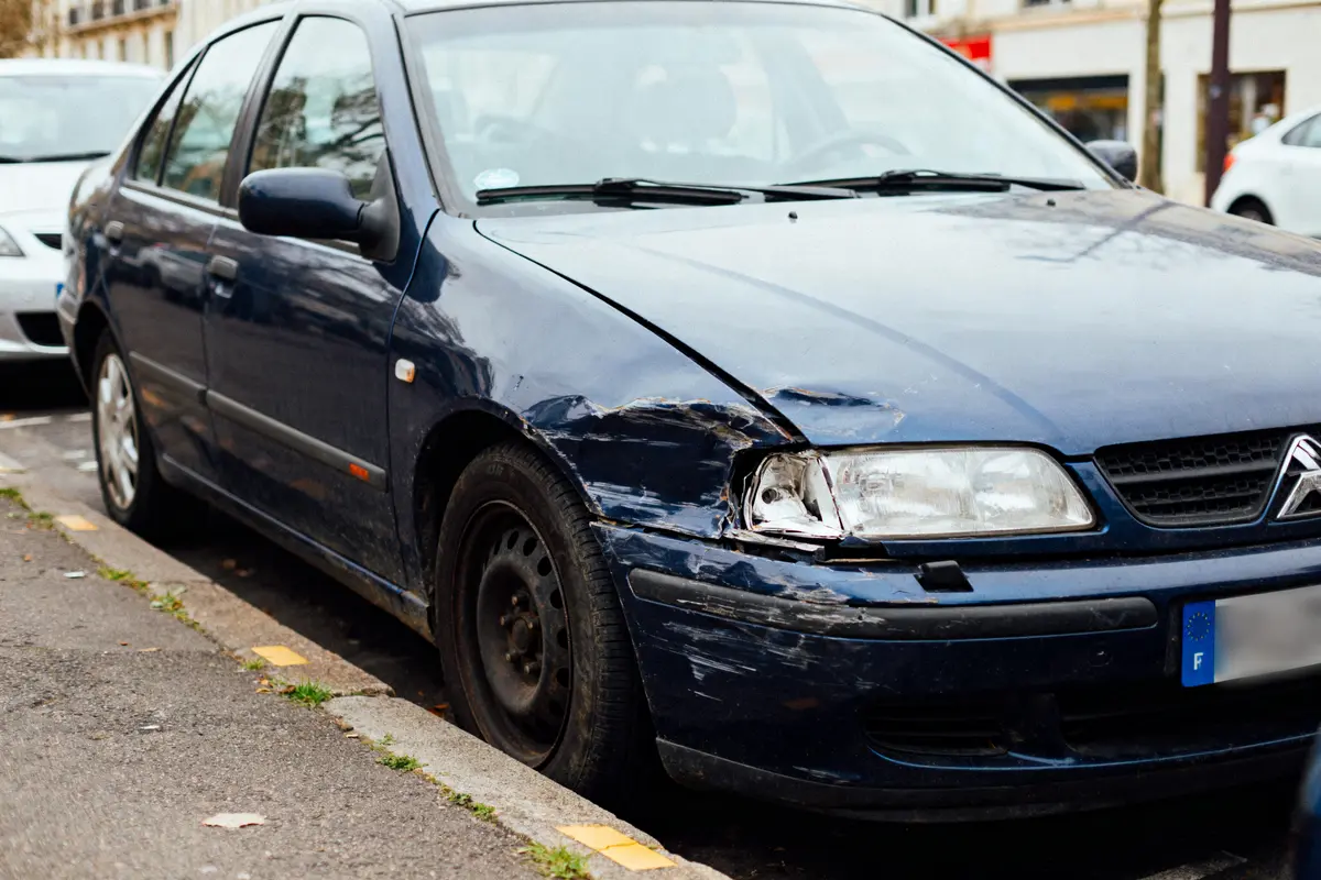Voiture bleue avec aile avant droite endommagée, stationnée en parallèle.