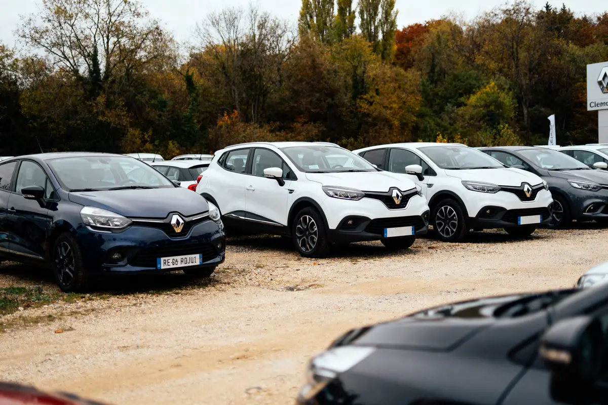 Plusieurs voitures Renault garées sur un parking, entourées d'arbres aux couleurs automnales.