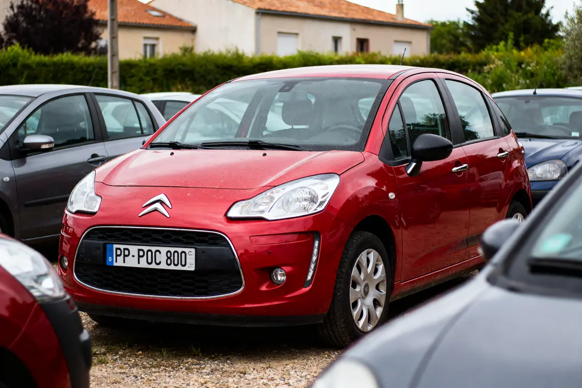 Voiture rouge Citroën garée dans un parking, entourée d'autres véhicules. Plaque d'immatriculation visible.