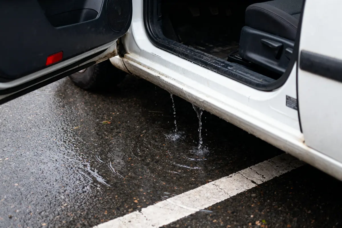 Porte de voiture ouverte, fuite d'eau sur le sol mouillé.