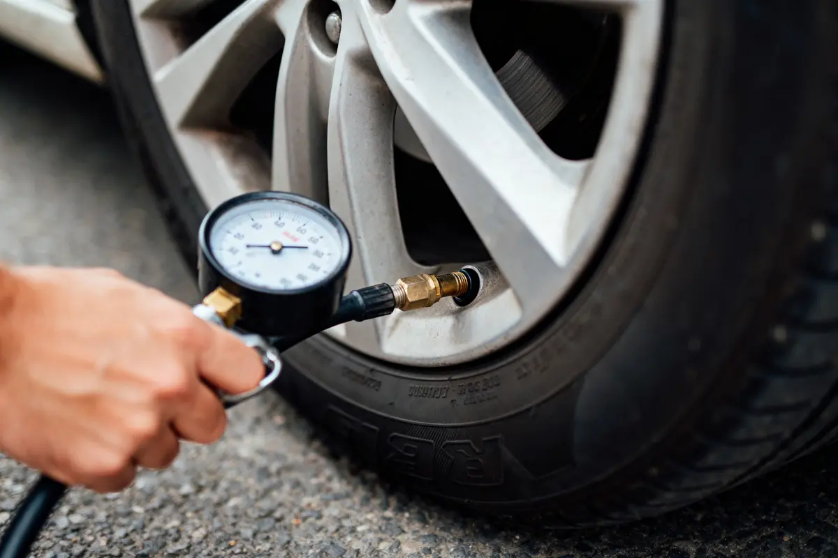 Main mesurant la pression d'un pneu de voiture avec un manomètre sur une route.