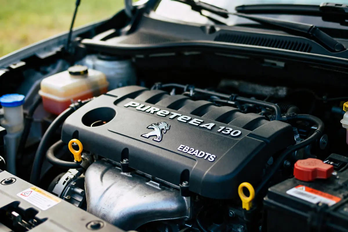 Moteur de voiture Peugeot PureTech 130, compartiment moteur, bouchon d'huile jaune visible, logo Peugeot.
