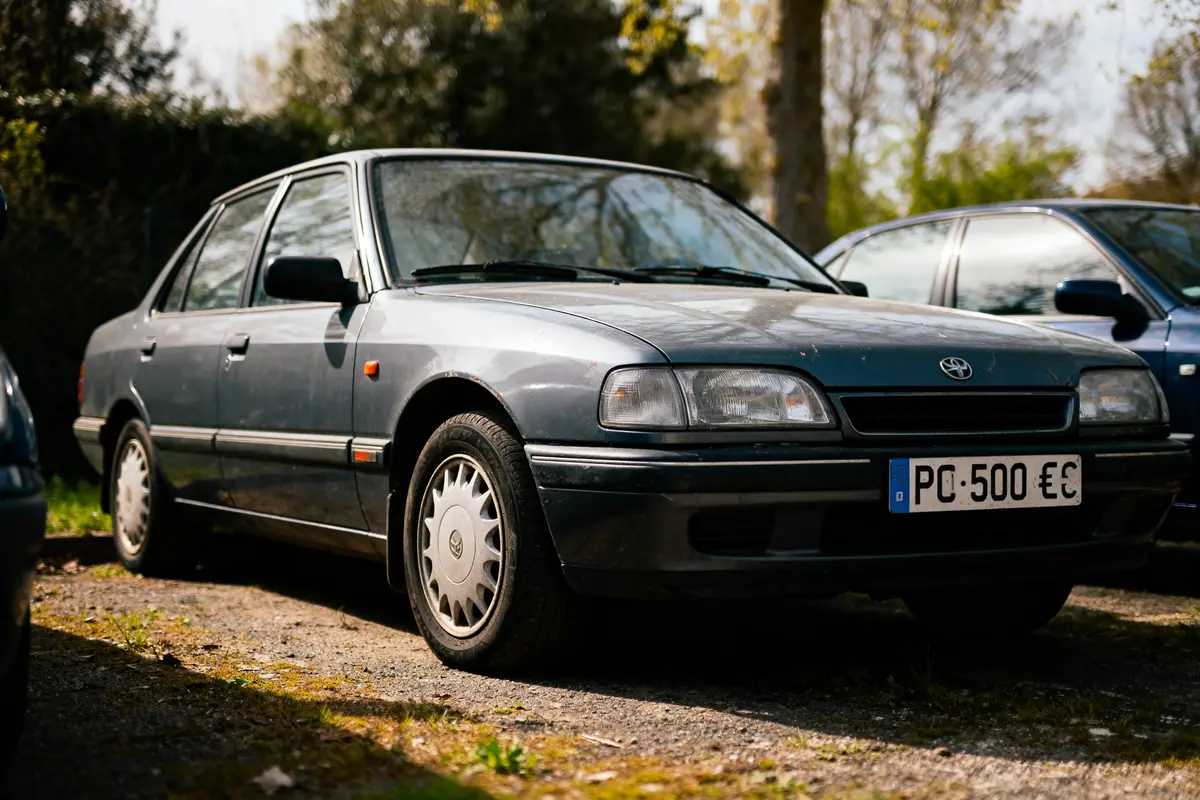 Voiture grise ancienne, garée à l'extérieur, avec plaque d'immatriculation mentionnant "PC-500 €€".