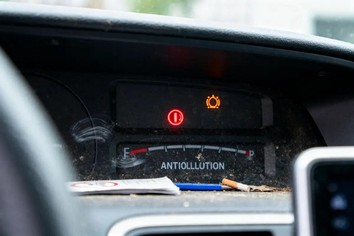 Tableau de bord de voiture avec voyant allumé, mégot de cigarette et saleté.