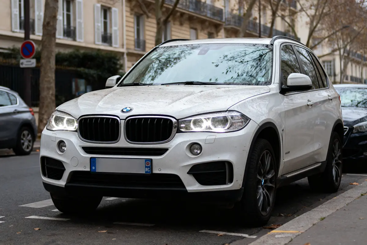 SUV BMW blanc stationné dans une rue urbaine avec immeubles en arrière-plan.