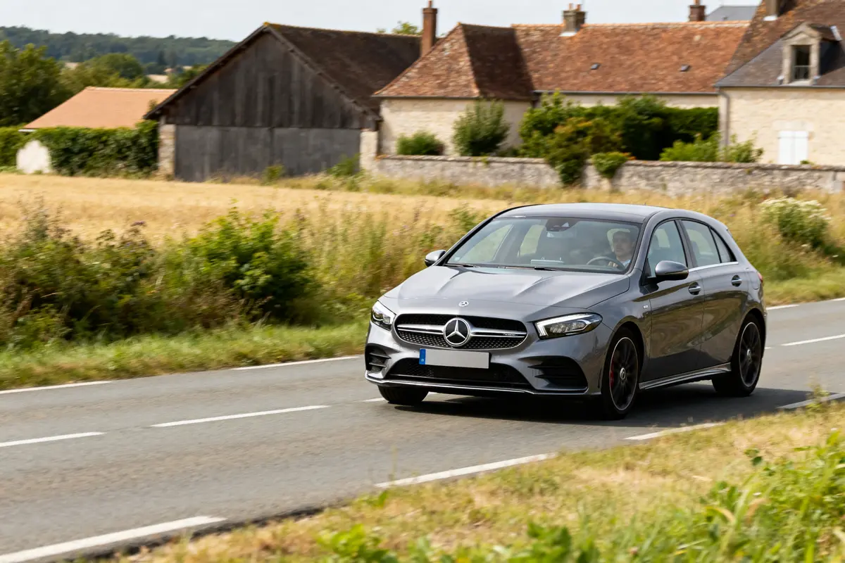 Voiture Mercedes Classe B grise roulant sur une route de campagne près de maisons anciennes