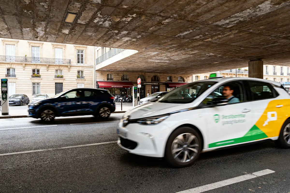 Taxi blanc électrique roulant sous un pont à Paris, soulignant l'importance du turismo urbain