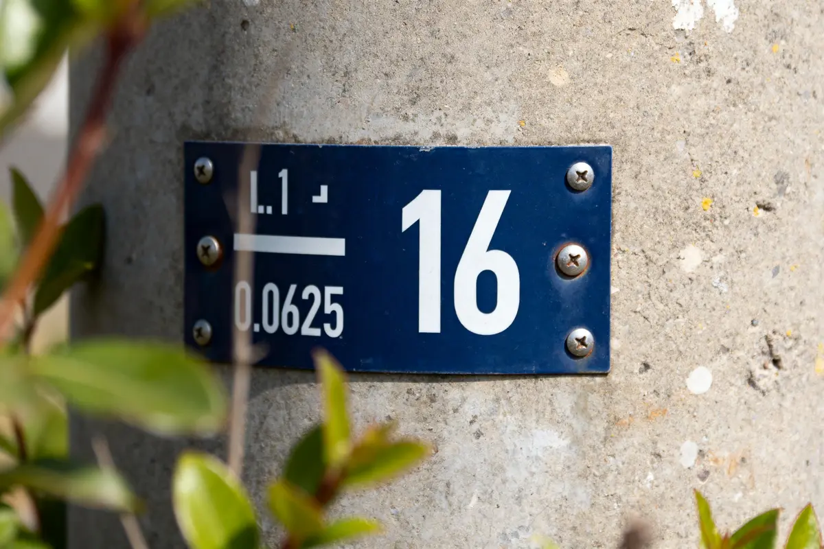 Plaque de signalisation bleue avec le chiffre 16 sur un mur en béton 1/16