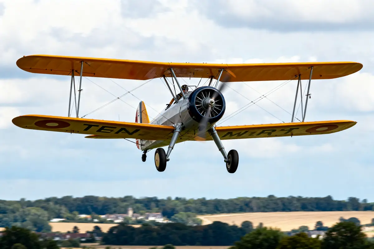 Avion biplan jaune volant au-dessus d'un paysage rural par temps nuageux