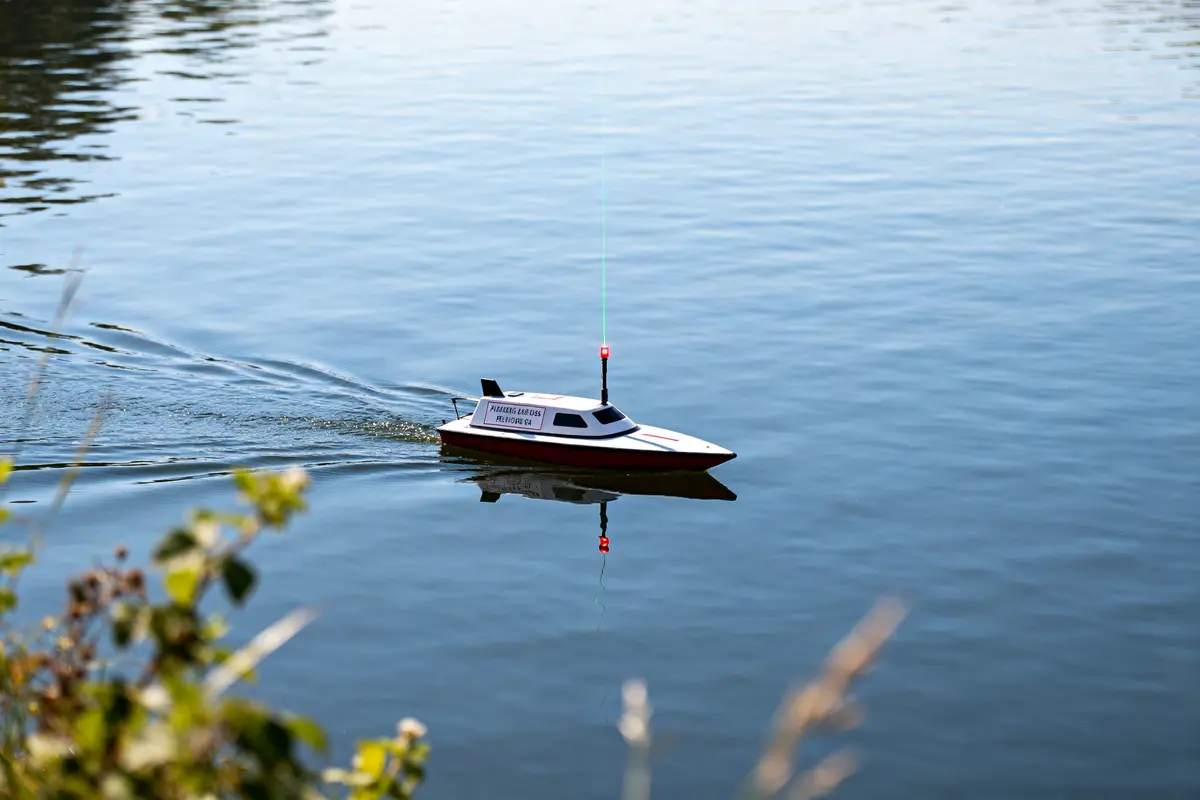 Petit bateau télécommandé naviguant, dériveur laser visible à la surface de l'eau