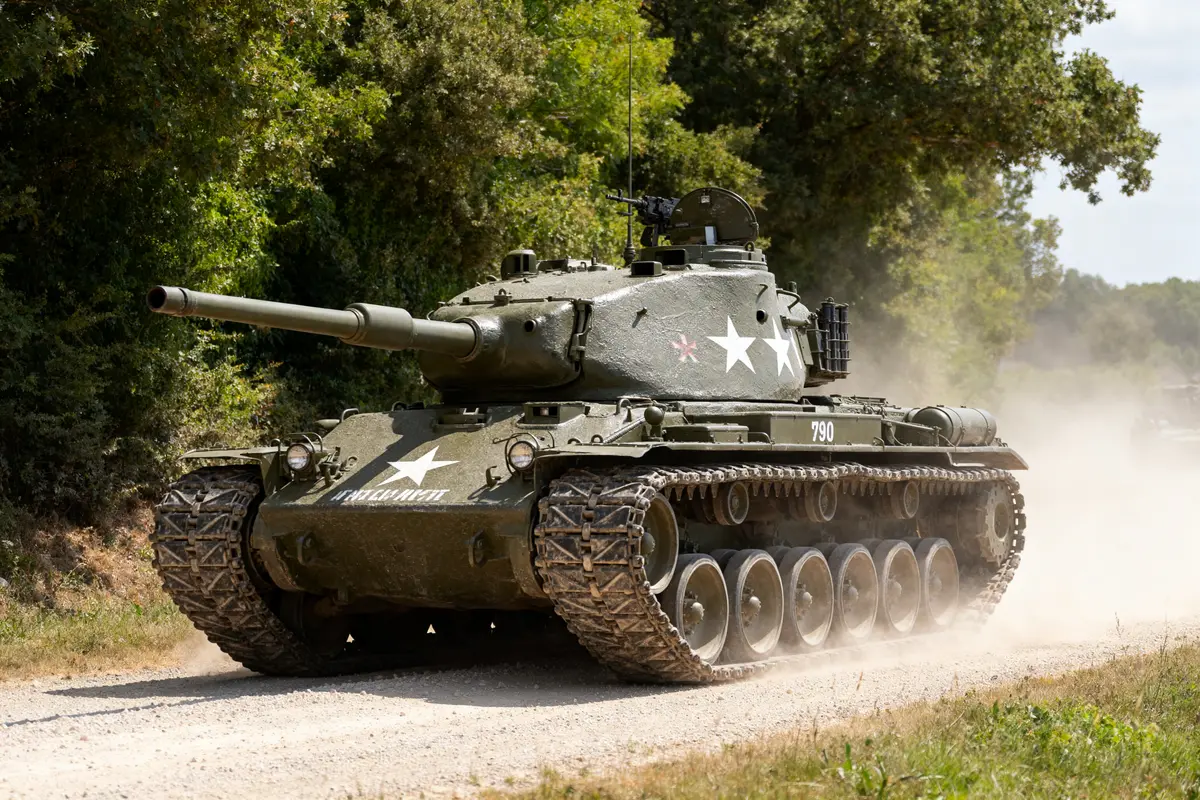 Char militaire Patton M47 en pleine avancée sur route poussiéreuse en forêt