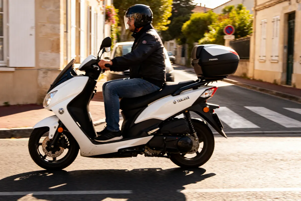 Homme conduisant un scooter Yamaha blanc dans une rue urbaine ensoleillée