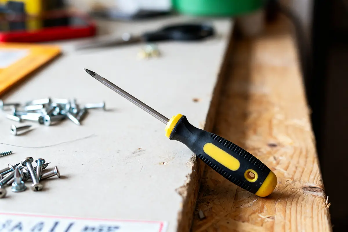Tournevis Tom Pouce et vis sur établi en bois lors d'un bricolage.